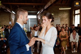 Bruid veegt een traan van haar wang tijdens een emotionele ringenwisseling op een prachtige indoorbruiloft in Grand-Sommartel, Zwitserland.